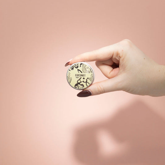 Hand holding a round product with 'Coconut' text against a pink background