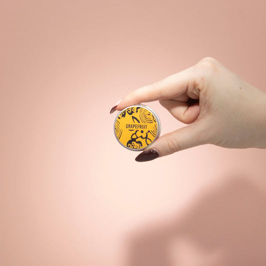 Hand holding a small round container with a yellow label on a pink background