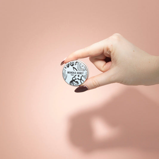 Hand holding a Manuka Honey product container against a pink background