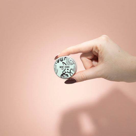 Hand holding a small round container with a brand logo against a pink background