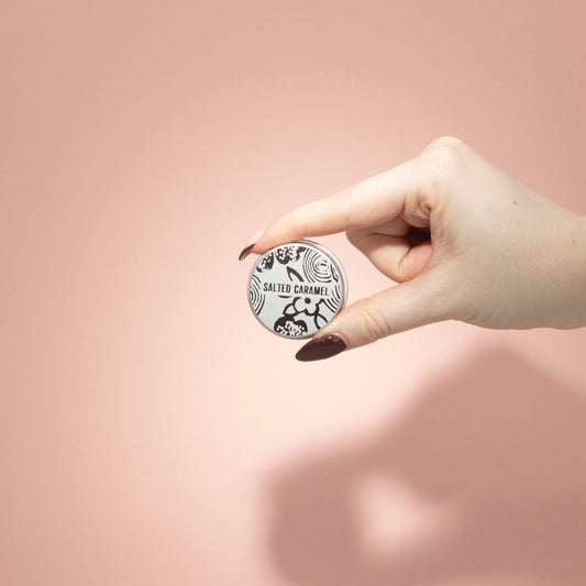 Hand holding a round salted caramel product against a pink background