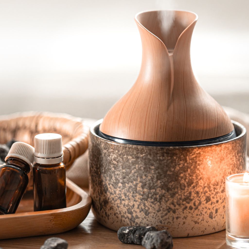 A wooden aromatherapy diffuser with essential oil bottles and a candle on a wooden surface.