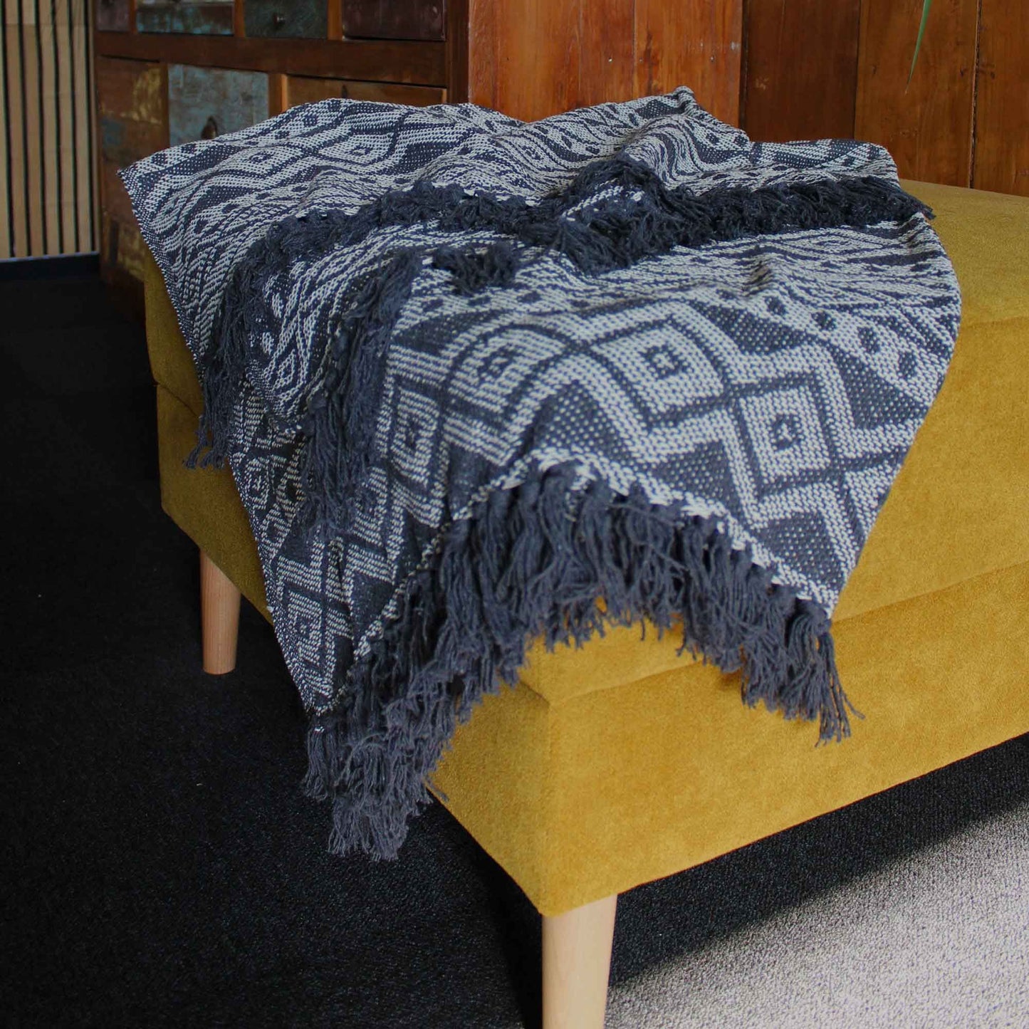 Blue patterned throw blanket draped over a yellow couch in a room with wooden paneling.