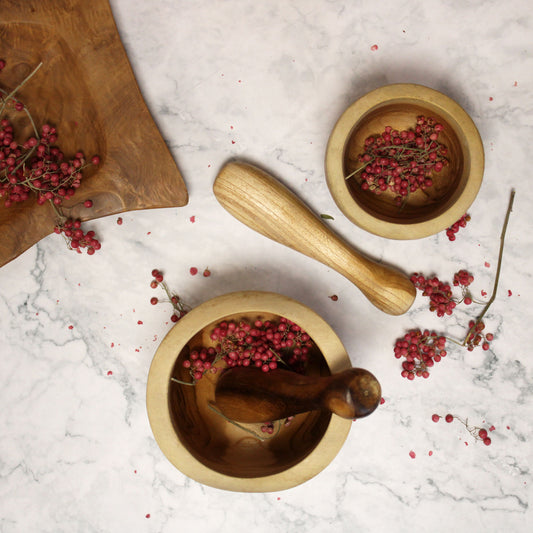 Wooden mortar and pestle with red berries on a marble surface