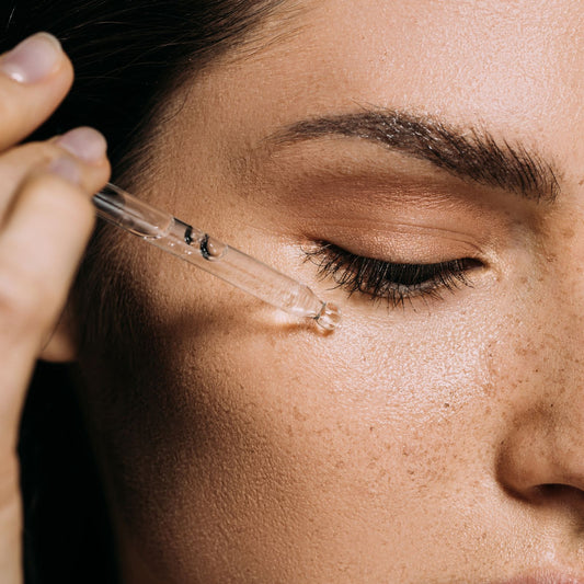 Close-up of a woman applying a dropper to her eye area.