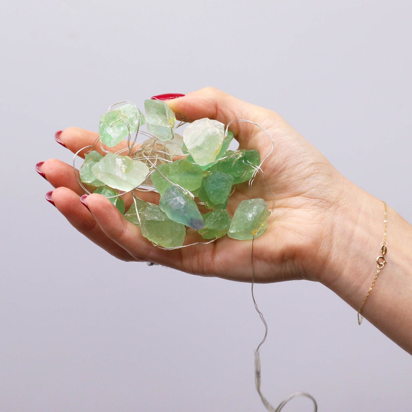 Hand holding a string of green sea glass against a plain background