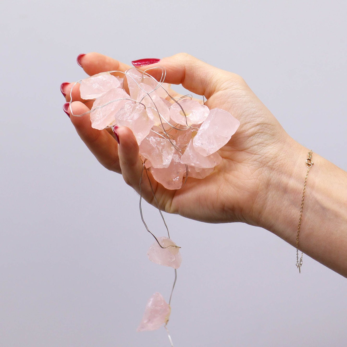 Hand holding a string of pink crystal beads against a light gray background