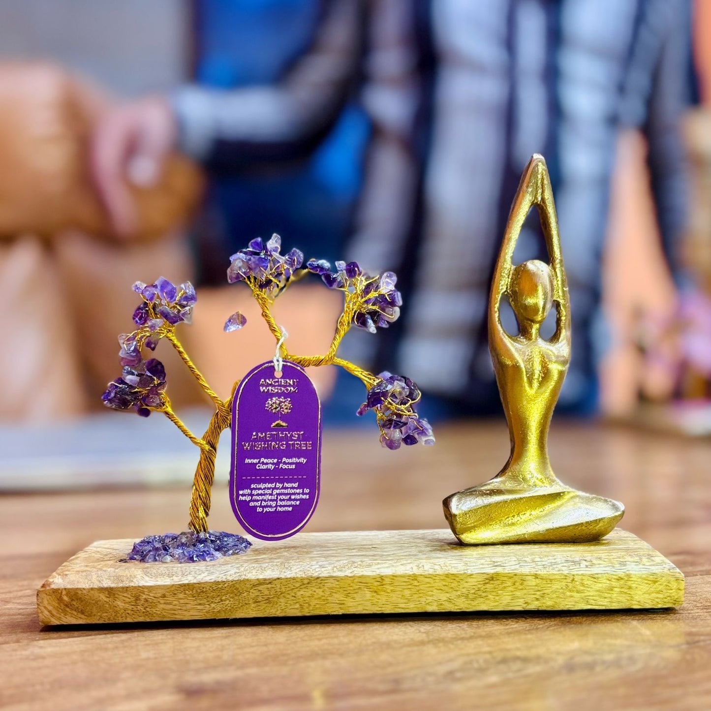 Decorative item with gold figure and purple tree on a wooden base, featuring 'Amethyst Wellness' branding.