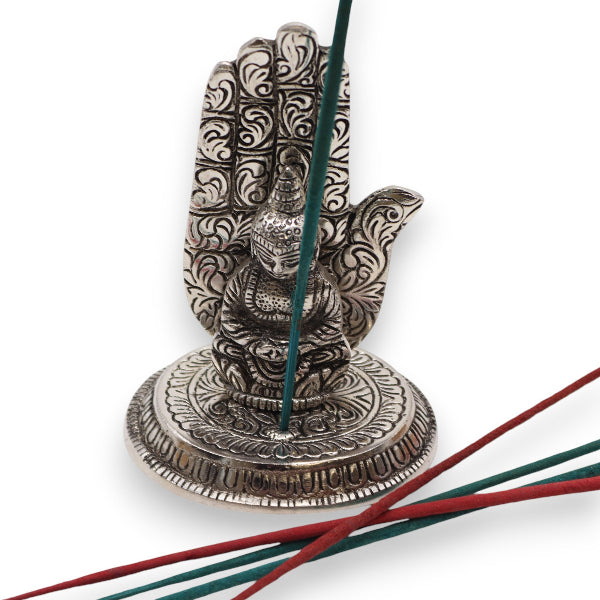 Decorative metal hand incense holder with incense sticks on a white background