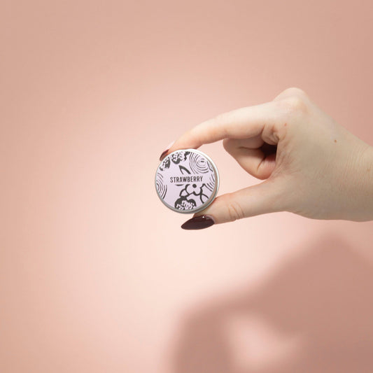 Hand holding a small round container with a strawberry design on a pink background