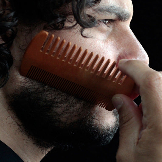 Man combing his beard with an orange comb against a dark background