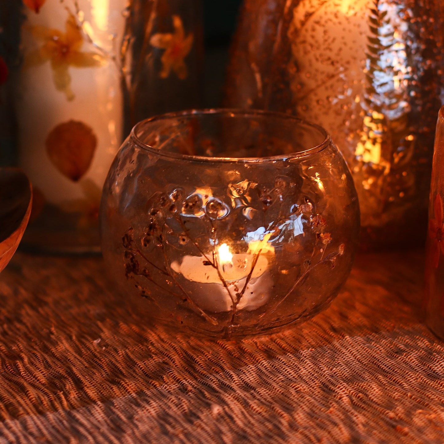 Glass candle holder with a lit candle on a textured surface