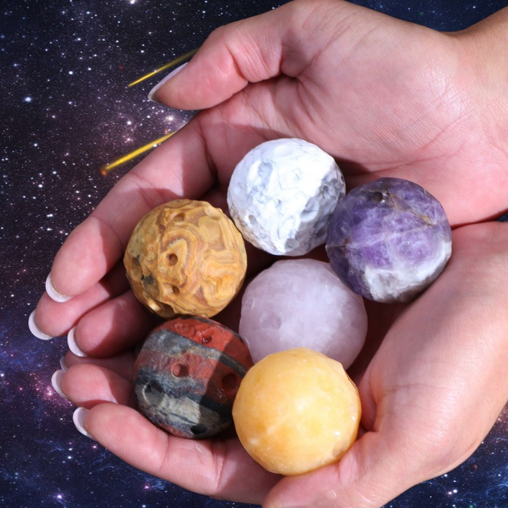 Person holding a selection of gemstone planets to show the size of each planet