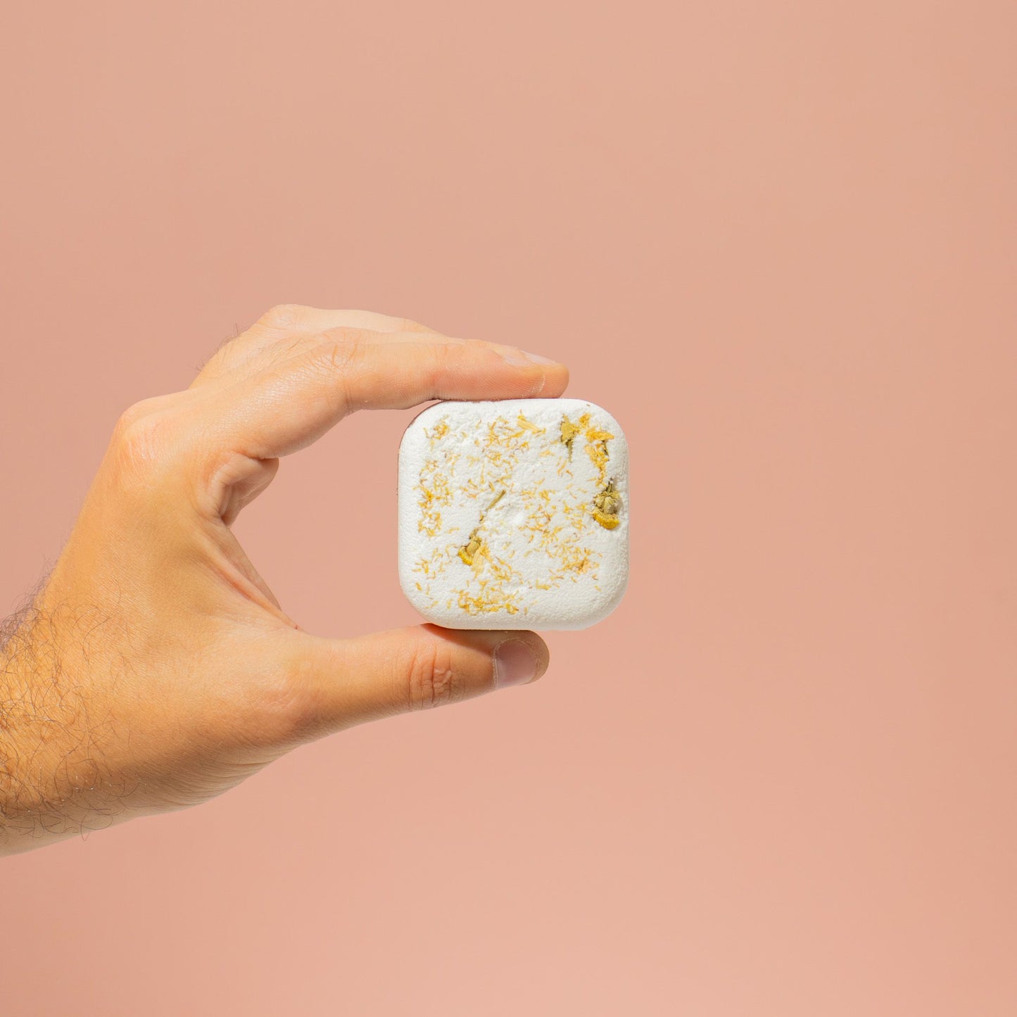 Hand holding a small white container with gold flakes against a beige background