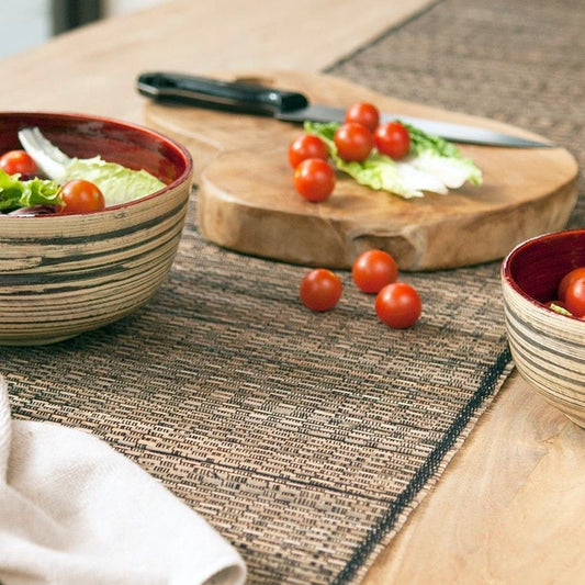 Bowl of salad with tomatoes and a wooden cutting board on a textured tablecloth.