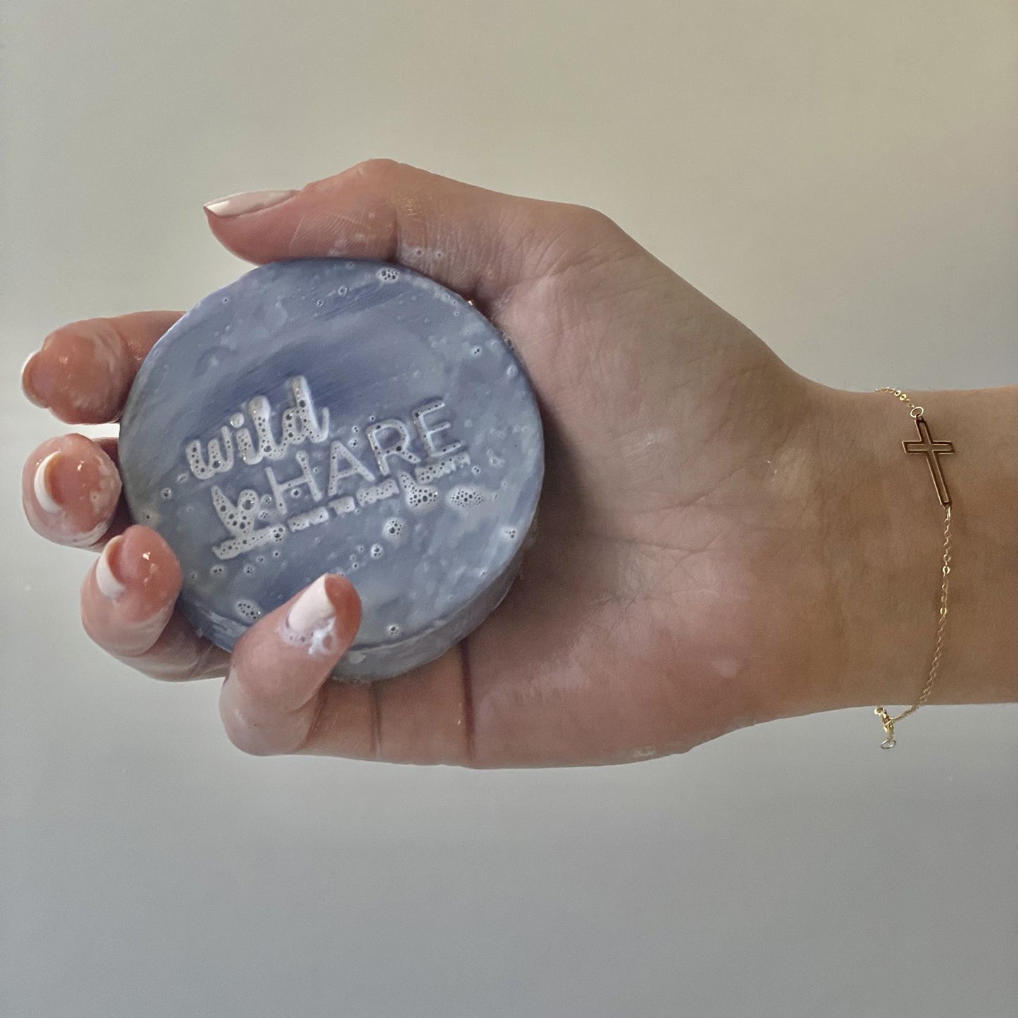 Hand holding a blue soap with 'wild hare' text against a plain background