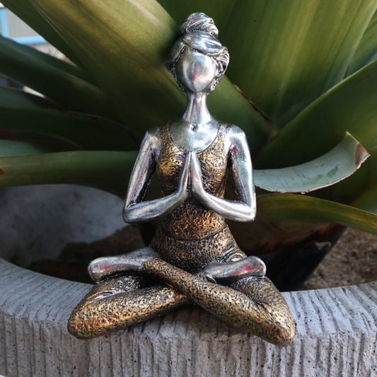 Decorative statue of a person in a meditative pose on a stone surface with green plants in the background.
