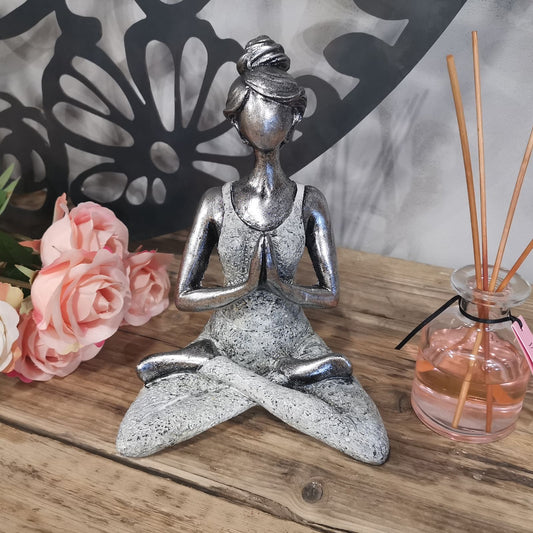 Silver yoga pose figurine on a wooden surface with flowers and a diffuser in the background