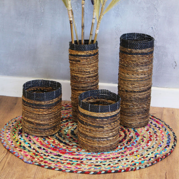 Set of woven vases on a colorful braided mat with a plain wall background