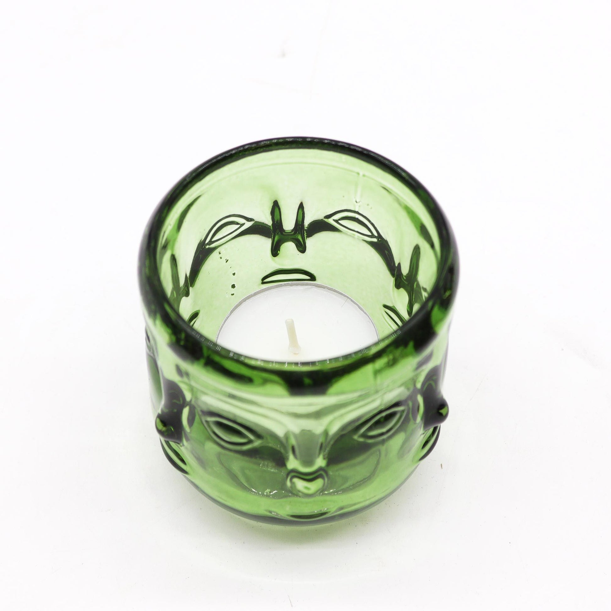 Green glass candle holder with buddha face design on a white background