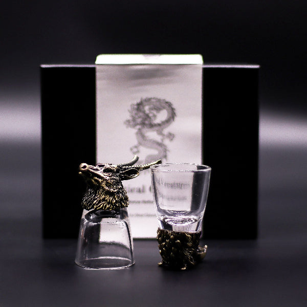 Two glass shot glasses with bronze deer heads on a dark background