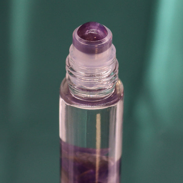 Roll-on bottle with purple cap and clear body on a green background