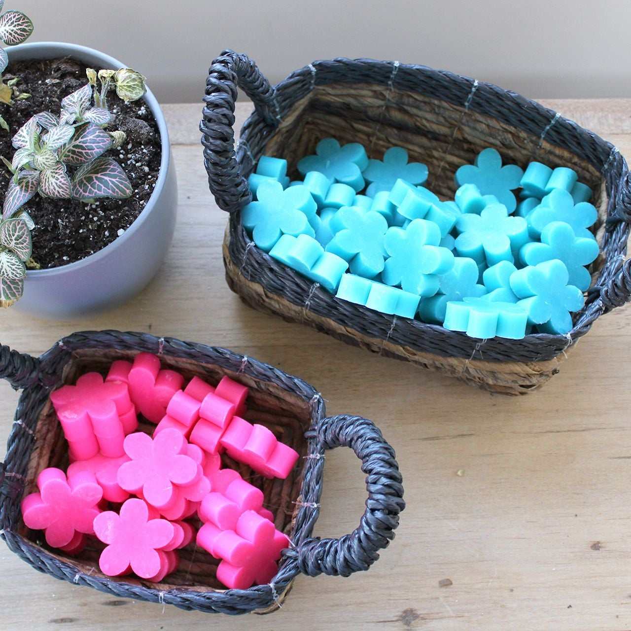Two woven baskets filled with pink and blue flower-shaped objects on a wooden surface.