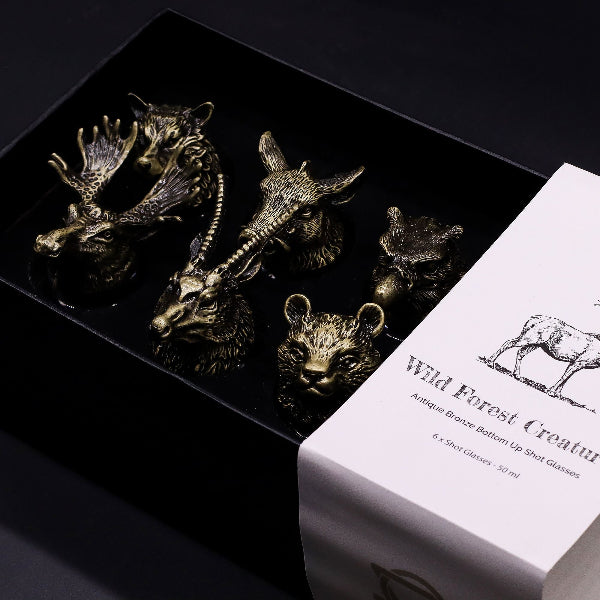 Set of bronze animal-shaped shot glasses on a black tray with a branded box.