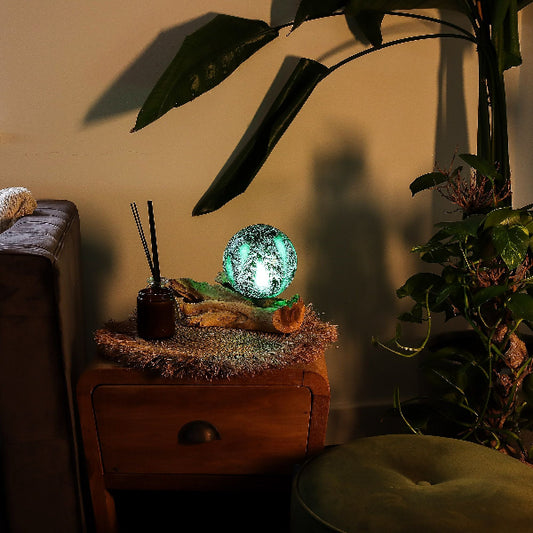 Decorative lamp on a wooden surface with plants and a couch in the background