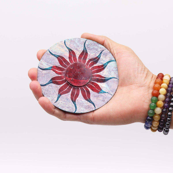 Hand holding a round, sun-shaped object with colorful design on a white background