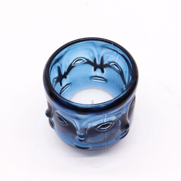 Blue glass candle holder with face design on a white background