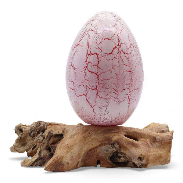 Pink ceramic egg with cracked texture on a wooden base against a white background