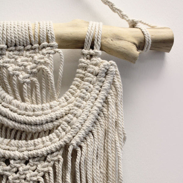 Macrame wall hanging with natural wood rod on a light background