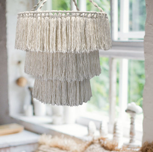 Macrame hanging plant holder with tassels in a room with a window.