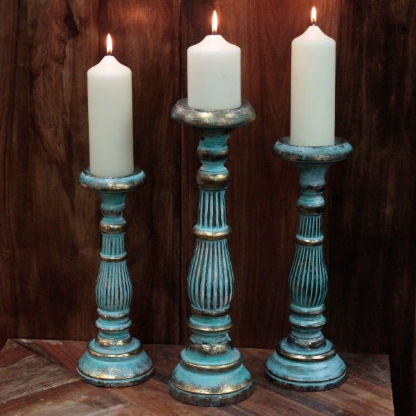 Three candlesticks with white candles on a wooden surface against a dark wooden background