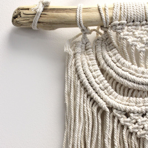 Close-up of a macrame wall hanging with natural wood stick on a white background