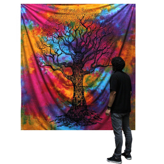 Person standing in front of a colorful tie-dye tapestry with a tree design.