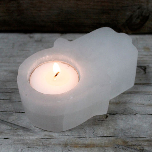 Tealight candle in a white stone hamsa holder on a wooden surface