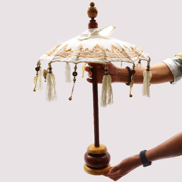 Decorative umbrella with tassels held by a person against a white background