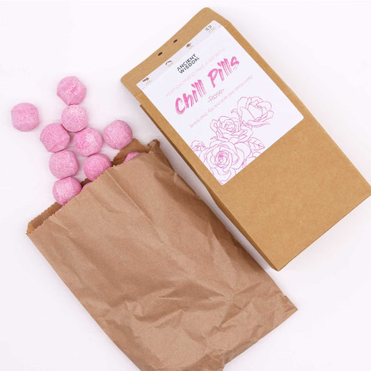 Pink balls in an open brown paper bag with a branded box on a white background