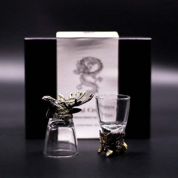 Two glass shot glasses with gold deer heads on a dark background