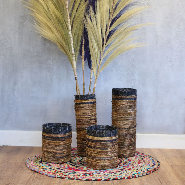 Set of woven vases with dried plants on a colorful rug against a gray wall.
