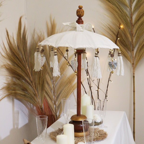 Decorative table setting with a white umbrella, candles, and glasses on a tablecloth.
