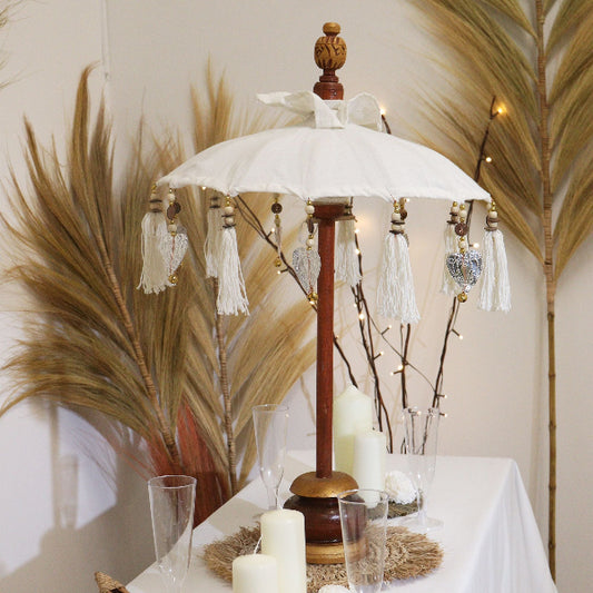 Decorative table setting with a white umbrella, candles, and glasses on a tablecloth.