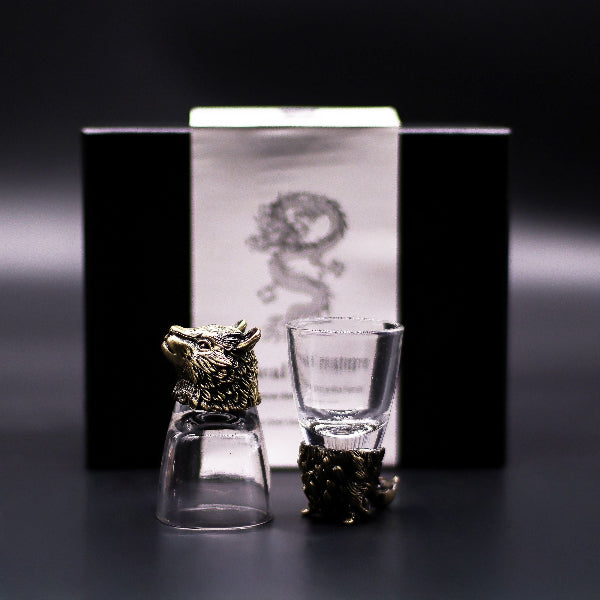 Two glass shot glasses with animal-shaped holders in front of a branded box on a dark background