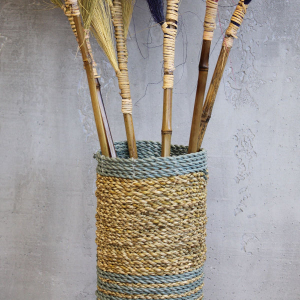 Woven vase with bamboo sticks against a gray concrete wall