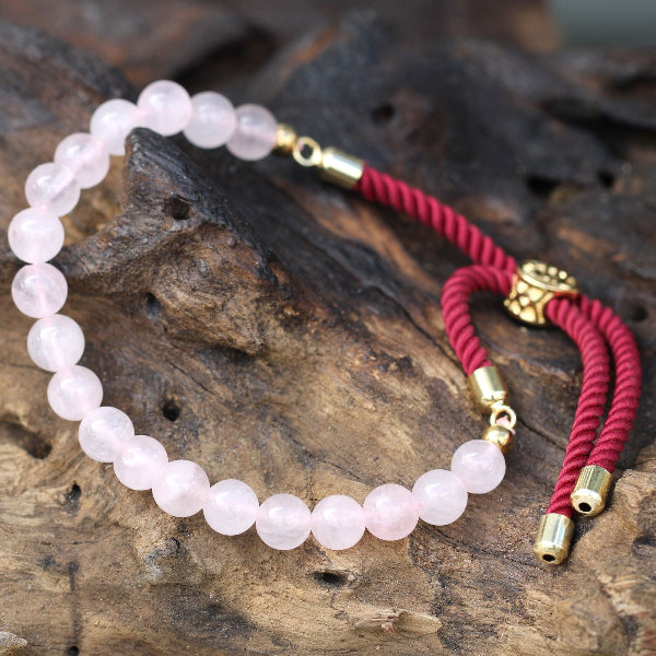 Rose quartz beaded bracelet with red cord and gold clasps on a wooden surface