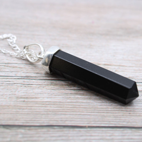 Black crystal pendant on a silver chain against a wooden background