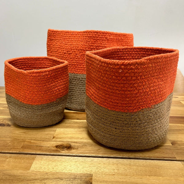 Three orange and brown woven baskets on a wooden surface.