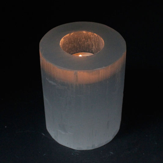 Cylindrical selenite candle holder with a candle inside on a black background